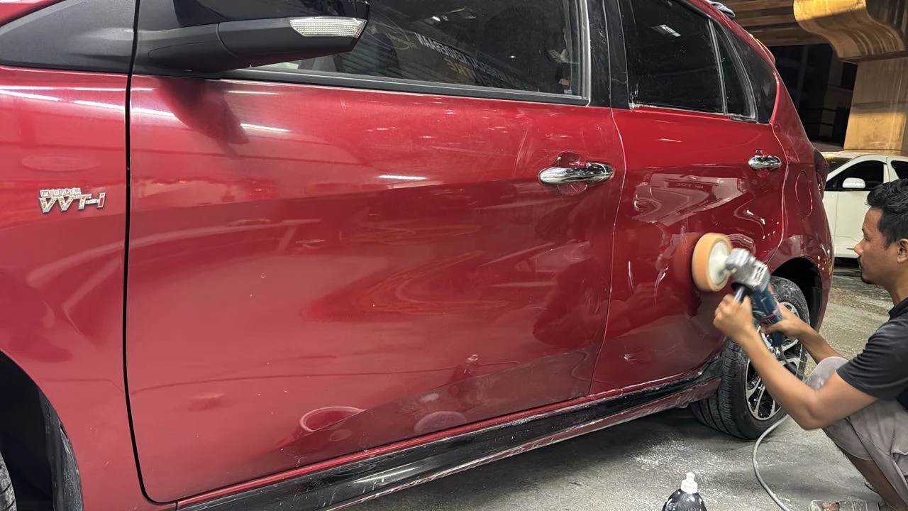 A technician machine-polishing the rear side panel of a red MPV